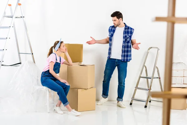 Boyfriend showing shrug gesture and looking at girlfriend sitting on boxes — Stock Photo
