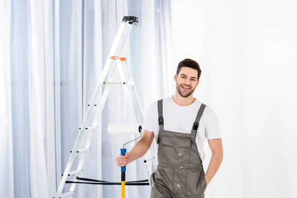 Sorrindo bonito homem de pé com pincel de rolo de pintura — Fotografia de Stock