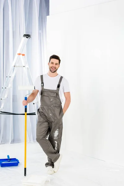 Sorrindo bonito homem de pé com pincel de rolo de pintura — Fotografia de Stock