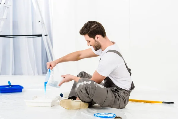 Side view of handsome man pouring paint into tray — Stock Photo