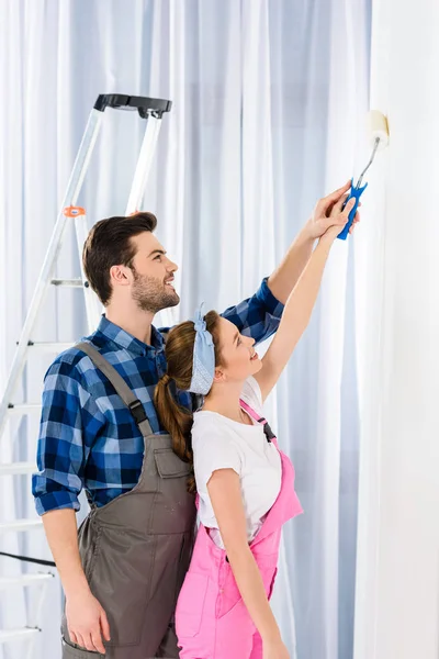 Novio ayudando novia pintura pared - foto de stock