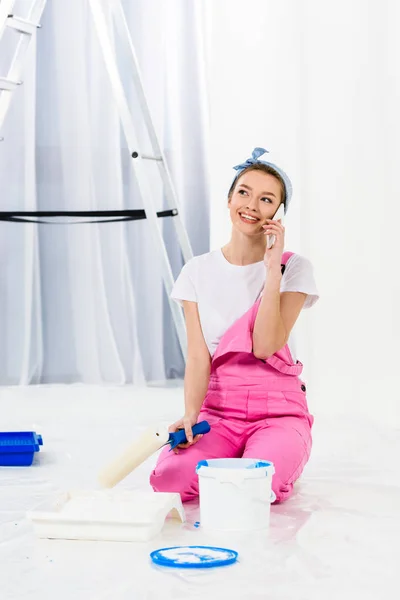 Smiling girl sitting with paint roller brush and talking by smartphone — Stock Photo