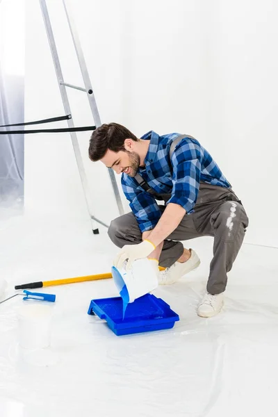 Homme souriant verser de la peinture du seau dans un bac à peinture en plastique — Photo de stock