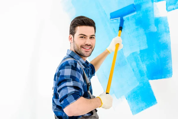 Sonriente hombre guapo pintura pared con pintura azul - foto de stock