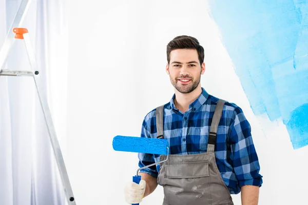 Sonriente hombre de pie con pincel de rodillo de pintura y mirando a la cámara - foto de stock