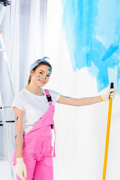 Sonriente chica sosteniendo pintura rodillo cepillo y mirando a la cámara - foto de stock