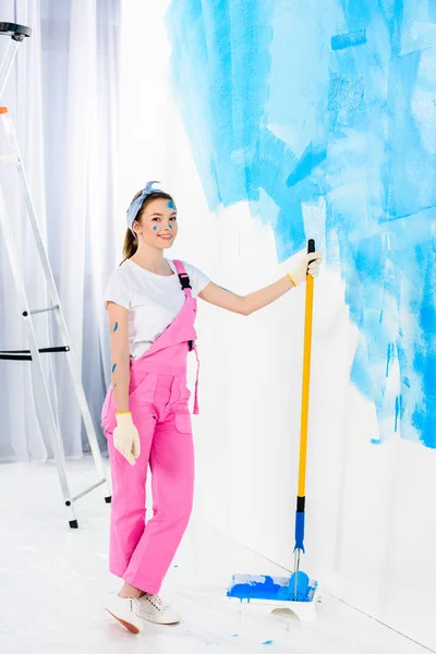 Menina sorrindo segurando pincel de rolo de pintura e olhando para a câmera — Fotografia de Stock