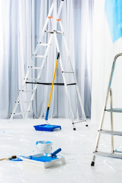Escaleras y pinceles de rodillo de pintura en pintura azul en la habitación - foto de stock