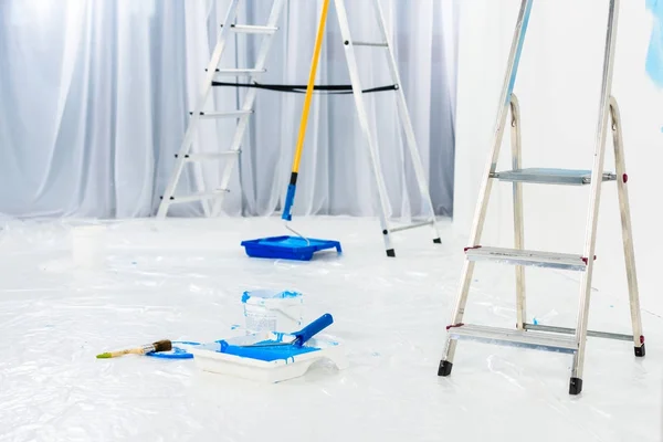 Escadas e pincéis de rolo de pintura em tinta azul no quarto — Fotografia de Stock