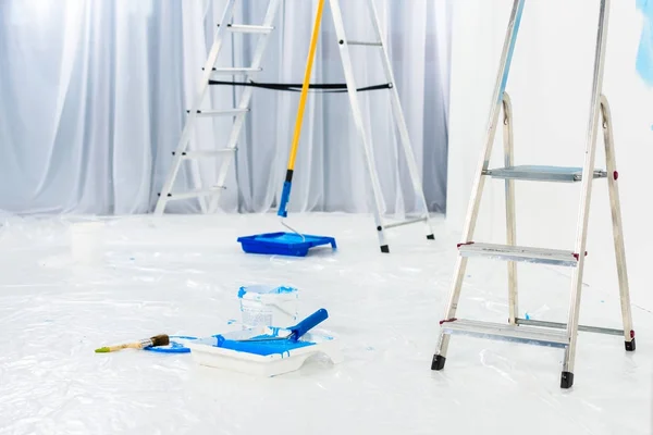 Échelles et pinceaux à rouleaux en peinture bleue dans la pièce — Photo de stock