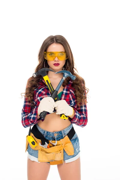 Beautiful girl in goggles and gloves with tool belt holding hammers, isolated on white — Stock Photo