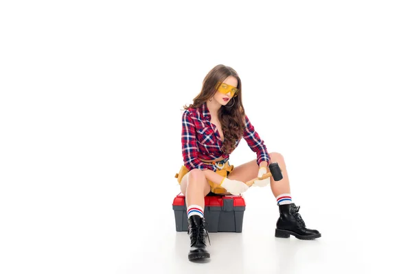 Attraktive sexy Mädchen sitzt auf Werkzeugkiste und hält Hammer, isoliert auf weiß — Stockfoto