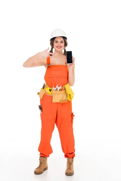 Trabalhador sorridente em uniforme apontando para smartphone com tela em branco, isolado em branco — Fotografia de Stock