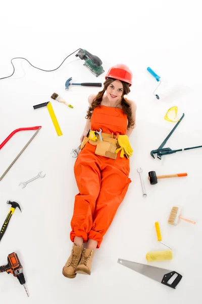 Overhead view of girl in overalls and hardhat lying on floor with different equipment and tools, isolated on white — Stock Photo