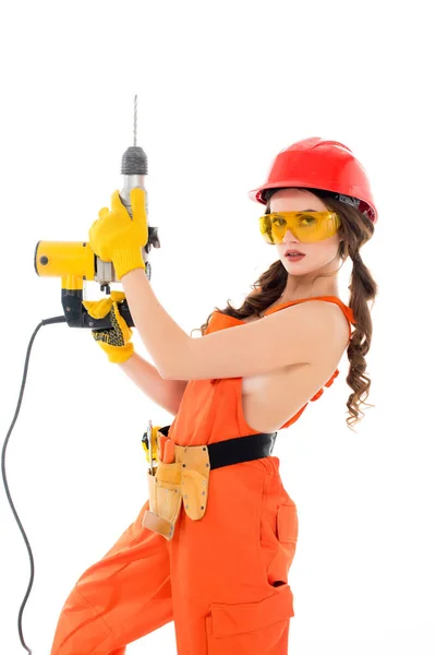 Mujer trabajadora en overoles y gorro de fuerza sosteniendo taladros eléctricos, aislado en blanco - foto de stock