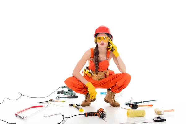 Femme de travail en salopette assise sur le sol avec différents équipements et outils, isolée sur blanc — Photo de stock