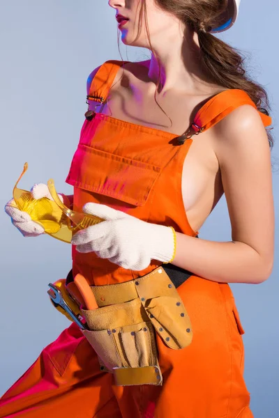 Cropped view of girl in overalls with tool belt and goggles, isolated on blue — Stock Photo