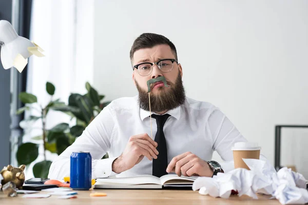 Retrato de hombre de negocios barbudo con decoración de fiesta sentado en el lugar de trabajo en la oficina - foto de stock