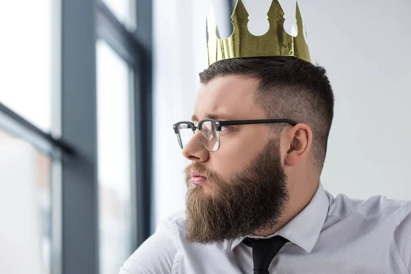 Портрет вдумчивого бизнесмена с бумажной короной на голове, смотрящего в сторону — стоковое фото
