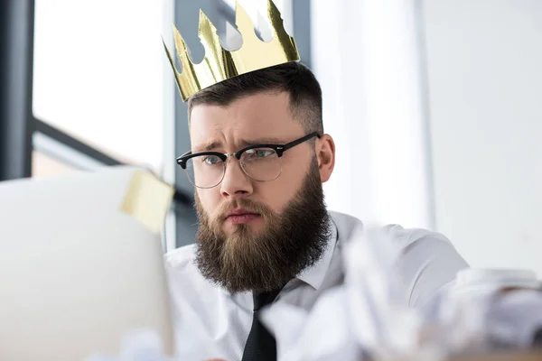 Retrato de homem de negócios com coroa de papel na cabeça trabalhando no laptop no escritório — Fotografia de Stock