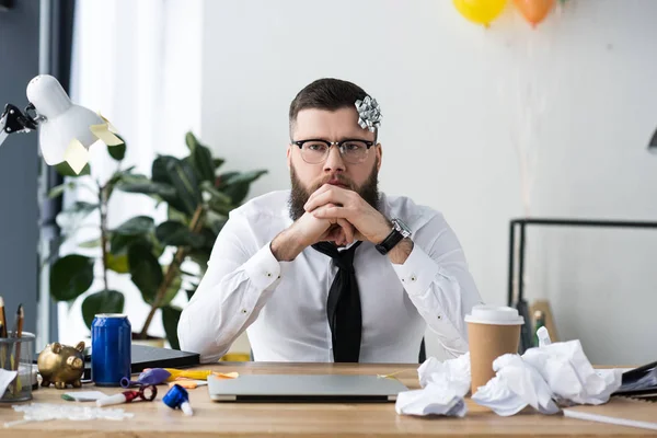 Portrait of pensive businessman with bow on head at workplace with laptop — Stock Photo