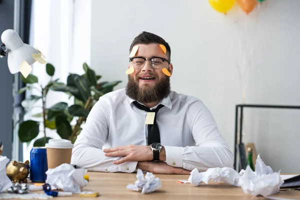 Retrato de hombre de negocios alegre en ropa formal con notas adhesivas en la cara en el lugar de trabajo en la oficina - foto de stock