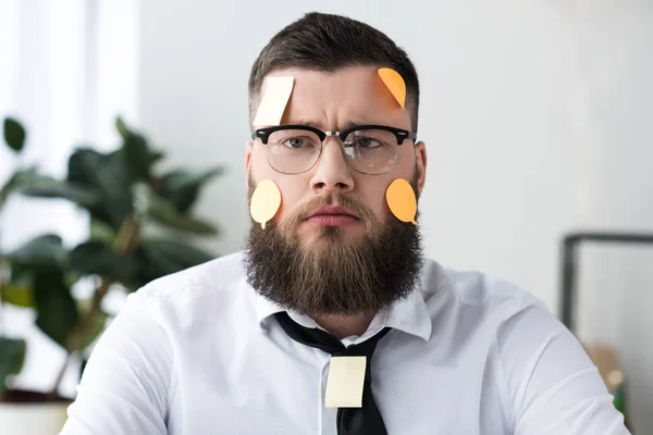 Portrait of serious businessman in formal wear with sticky notes on face — Stock Photo