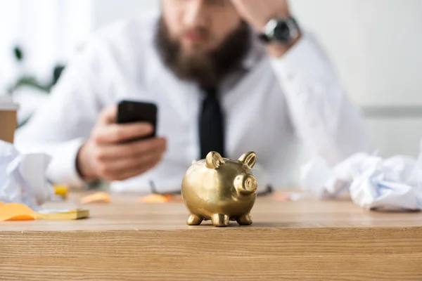 Selective focus of piggy bank and businessman with smartphone — Stock Photo