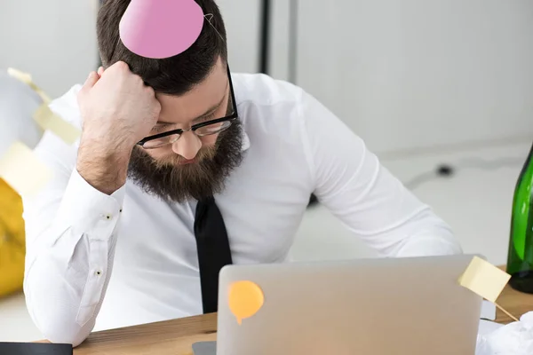 Empresario con cono de papel en la cabeza durmiendo en el lugar de trabajo - foto de stock