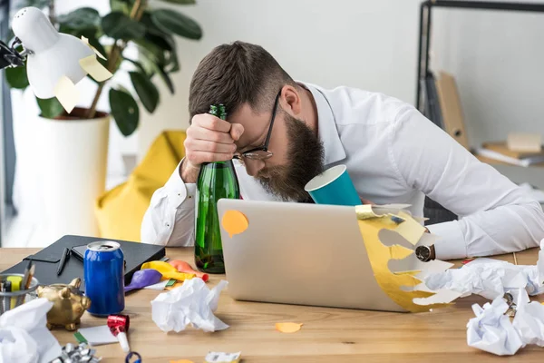 Drunk businessman with bottle of champagne sleeping at workplace with laptop — Stock Photo