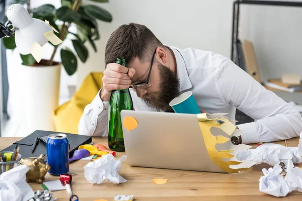 Empresario borracho con botella de champán durmiendo en el lugar de trabajo con portátil - foto de stock