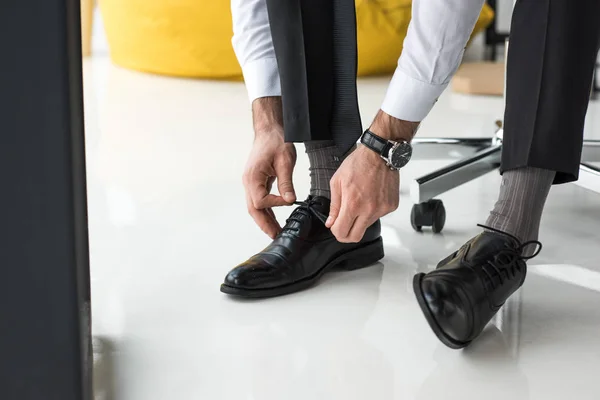 Teilsicht auf Geschäftsmann, der Schnürsenkel im Büro bindet — Stockfoto