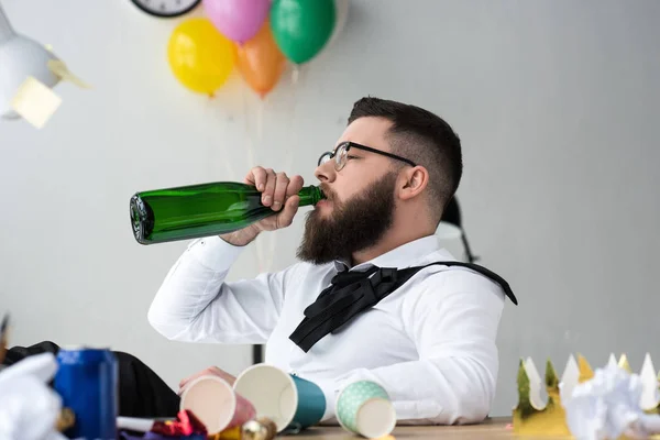 Homem de negócios barbudo bebendo champanhe de garrafa no local de trabalho no escritório — Fotografia de Stock