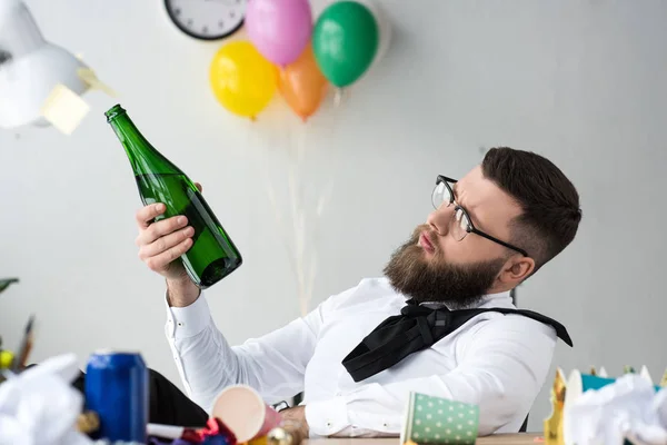 Hombre de negocios con botella de champán sentado en el lugar de trabajo en la oficina - foto de stock