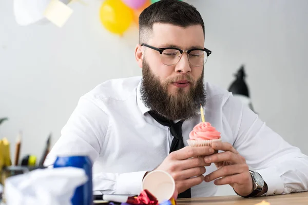 Бізнесмен дме свічку на день народження кекс на робочому місці в офісі — стокове фото