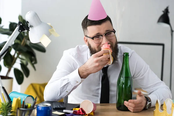 Ritratto di uomo d'affari in cono partito mangiare cupcake compleanno in ufficio — Foto stock