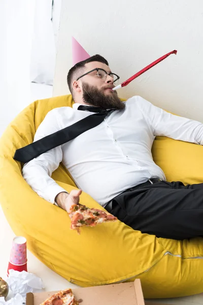 П'яний бізнесмен в офіційному одязі з паперовим конусом на голові відпочиває на мішкуватому стільці — стокове фото