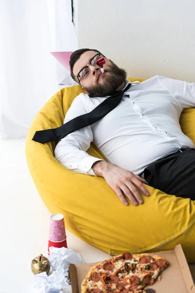 Drunk businessman in formal wear with paper cone on head resting on bag chair — Stock Photo