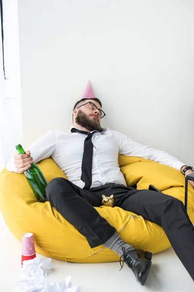 Пьяный бизнесмен в формальной одежде с бумажным конусом на голове, спящий на кресле — стоковое фото