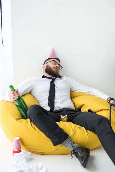 Hombre de negocios borracho en ropa formal con cono de papel en la cabeza durmiendo en la silla del bolso - foto de stock