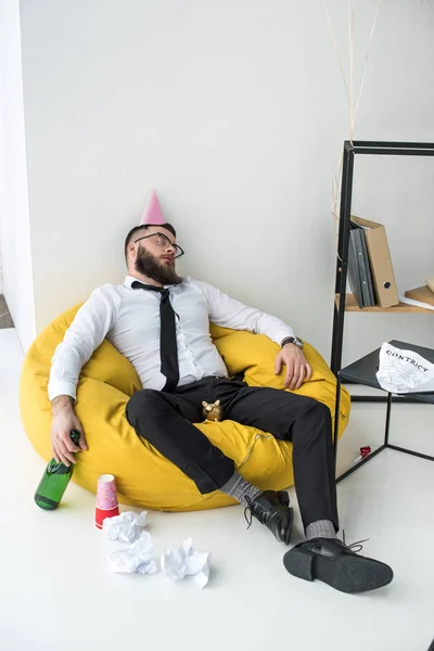 Drunk businessman in formal wear with paper cone on head sleeping on bag chair — Stock Photo