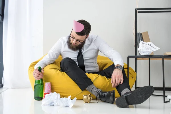 Drunk businessman in formal wear with paper cone on head sitting on bag chair — Stock Photo
