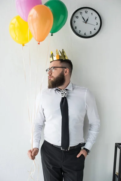 Portrait of businessman with paper crown on head and balloons looking away — Stock Photo