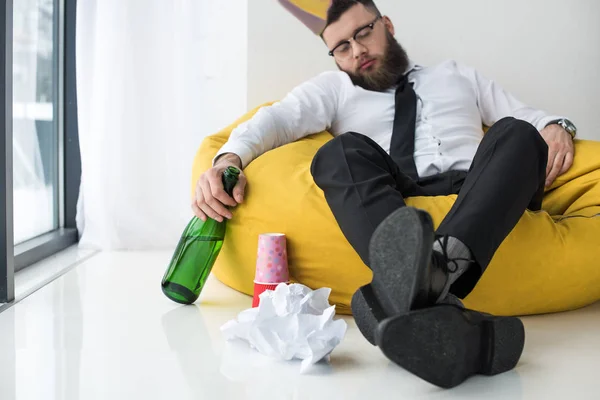 Drunk businessman in formal wear with bottle of champagne sleeping on bag chair — Stock Photo