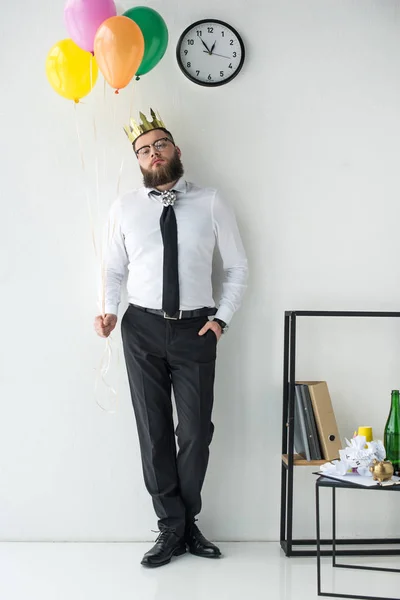 Homme d'affaires avec couronne en papier sur la tête et des ballons regardant caméra — Photo de stock