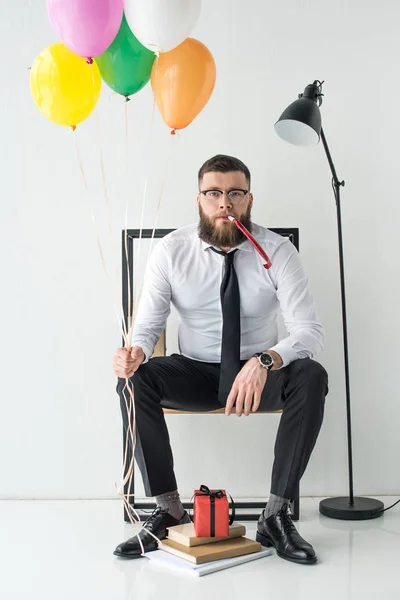Businessman in formal wear with balloons sitting on chair — Stock Photo