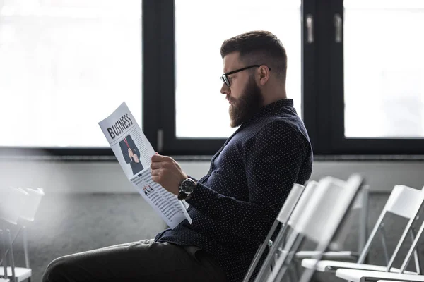 Seitenansicht eines konzentrierten Geschäftsmannes, der Zeitung liest, während er im Besprechungsraum sitzt — Stockfoto