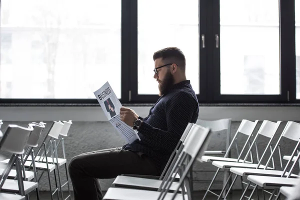 Вид збоку зосереджений бізнесмен читає газету, сидячи в кімнаті для переговорів — стокове фото
