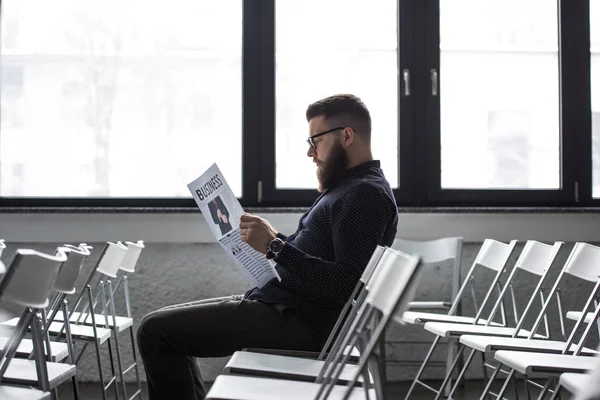 Vue latérale d'un homme d'affaires concentré lisant un journal assis dans une salle de réunion — Photo de stock