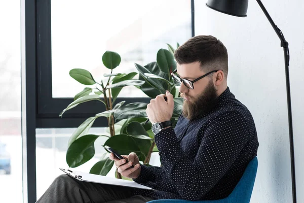 Vista lateral del hombre de negocios con bloc de notas utilizando el teléfono inteligente — Stock Photo
